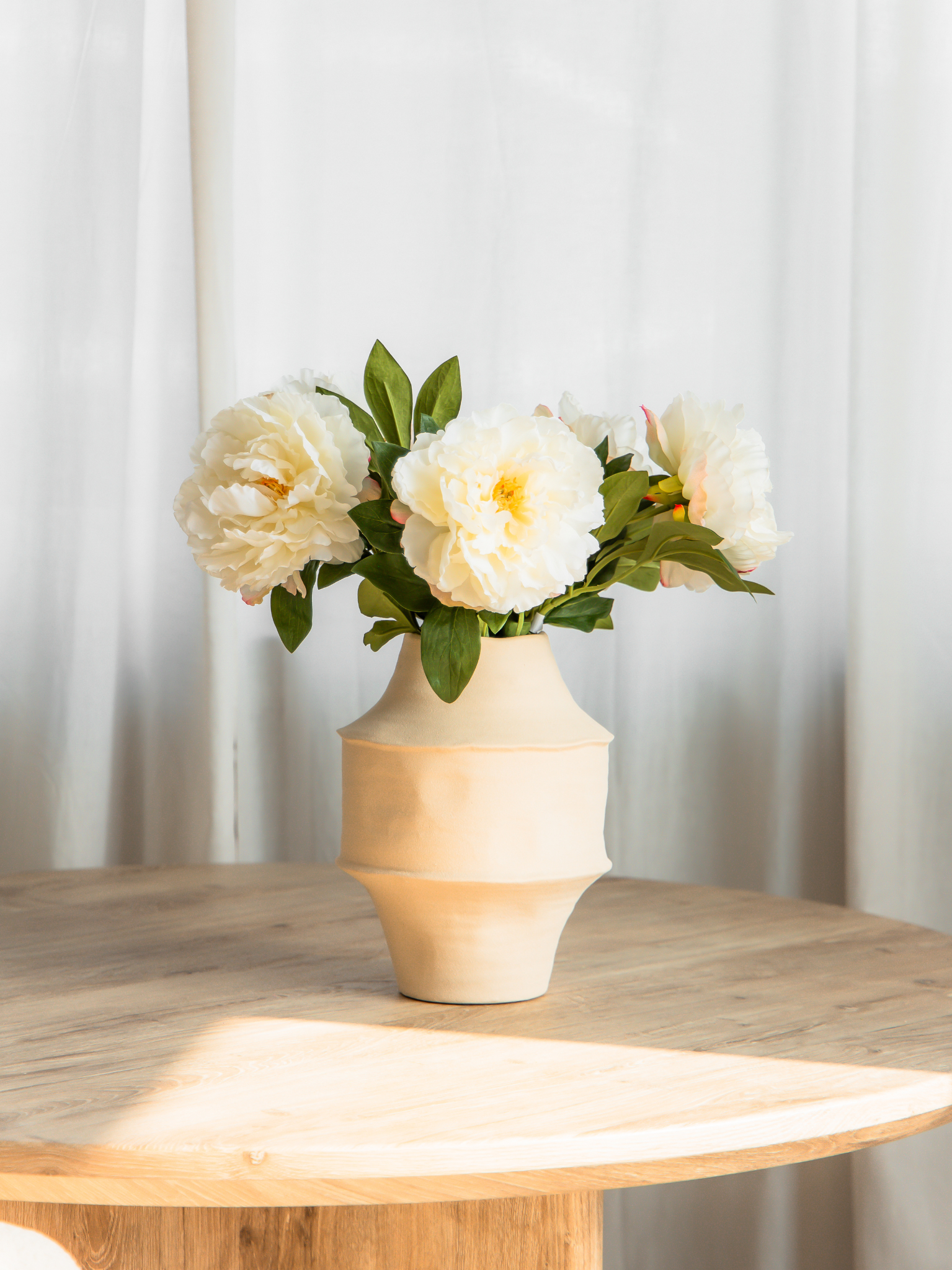5 witte zijden pioenrozen in beige vaas op eettafel