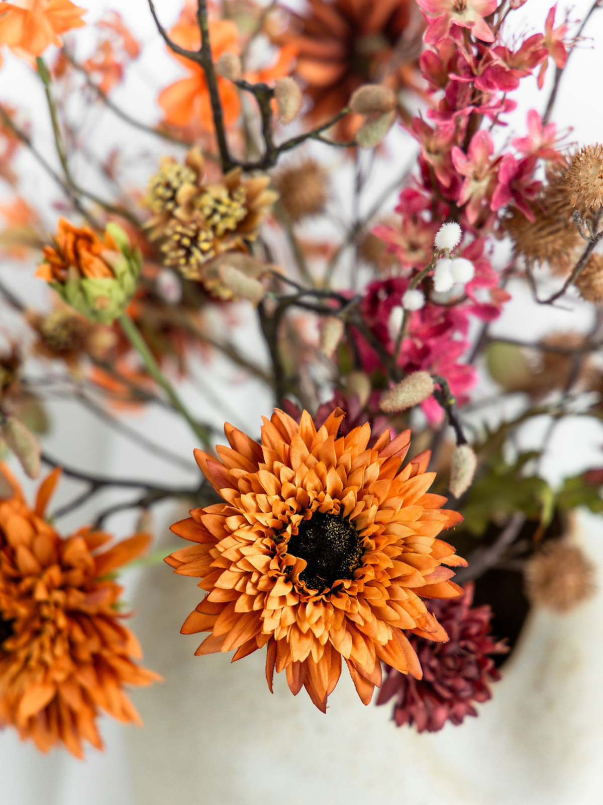 Close-up van grote oranje zijden chrysant met roze kunstbloemen en warme herfsttakken in boeket Amber.