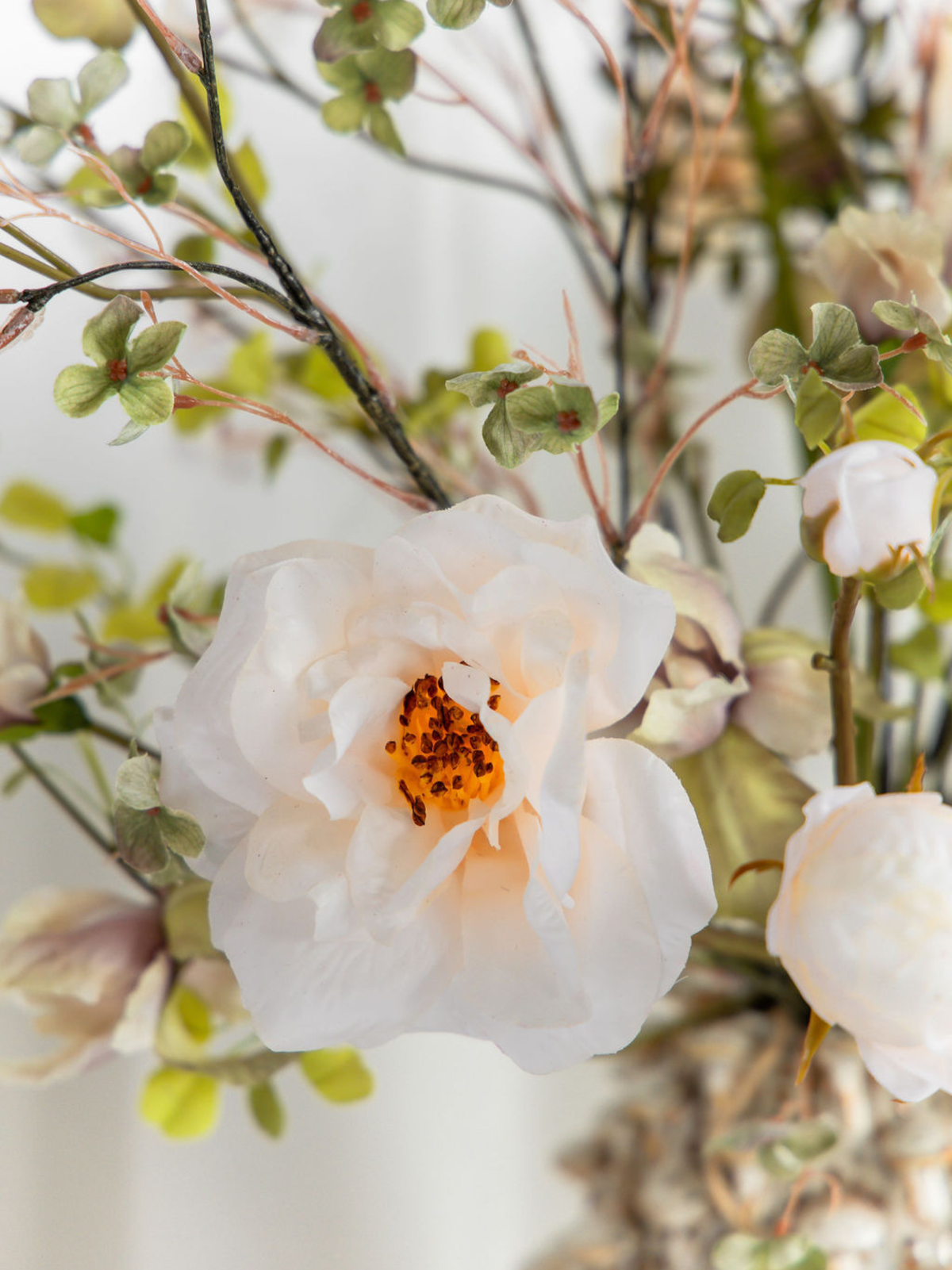 Close-up van een crèmekleurige zijden roos met groene bloesemtakken in kunstboeket Suus van Blossig Bloemen.