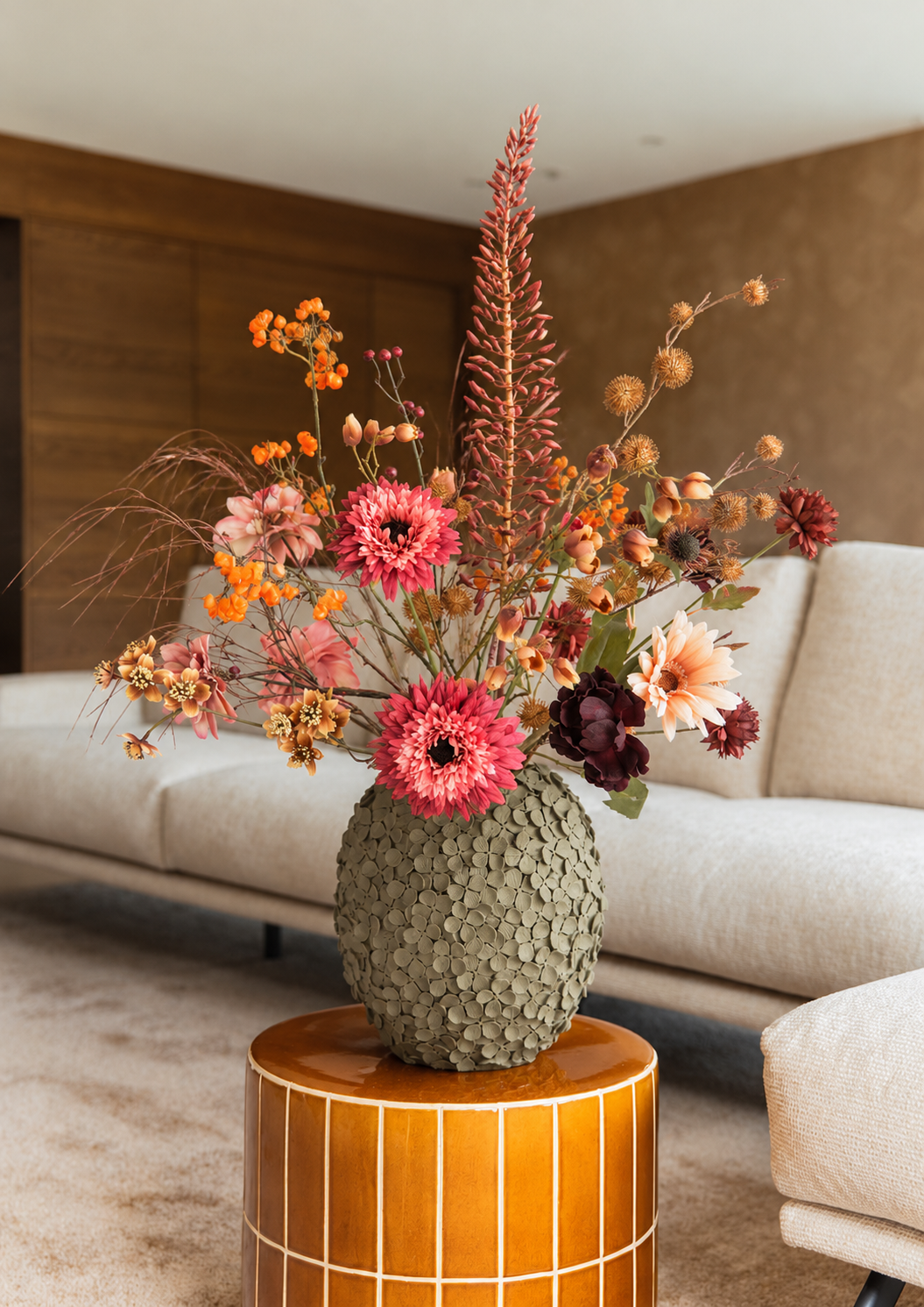 Groot zijden herfstboeket Amelie met oranje, roze en bordeauxrode kunstbloemen op een bijzettafel in een warme, moderne woonkamer.