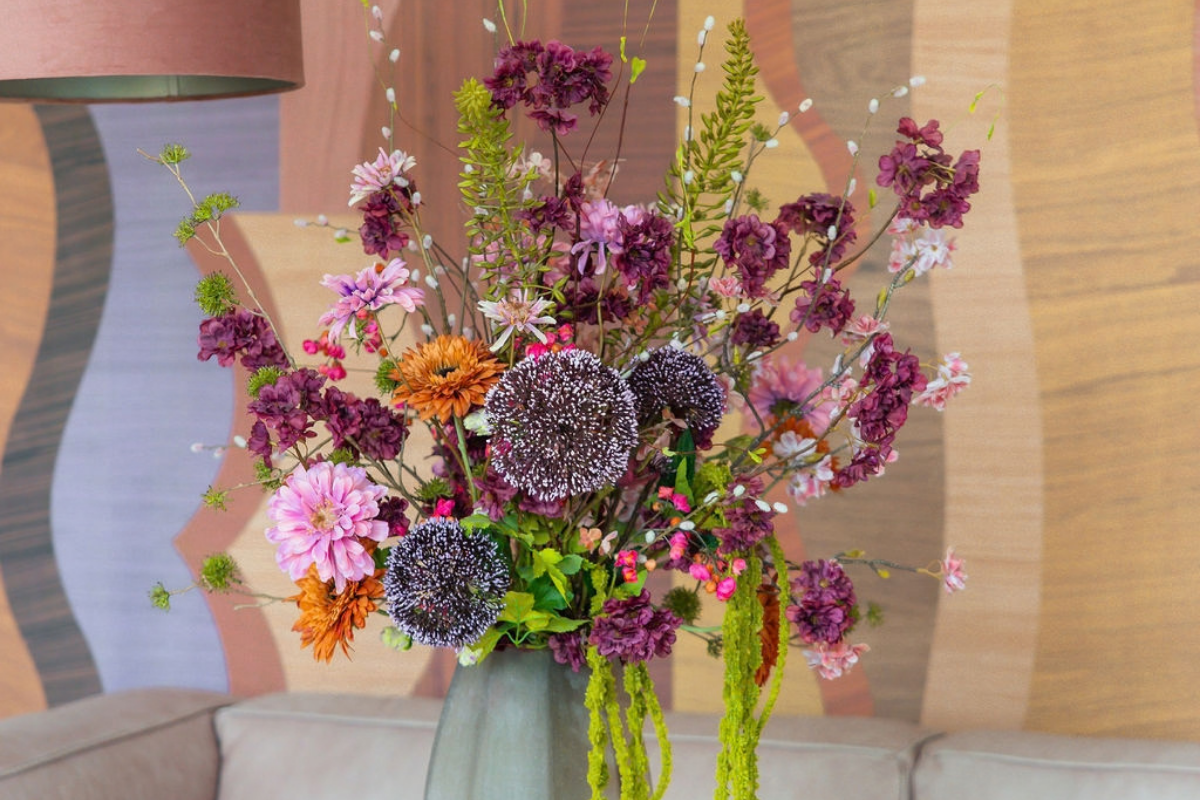 Kleurrijk zijden herfstboeket met burgundy, roze, oranje en groene kunstbloemen in een groene vaas als herfstdecoratie voor het interieur.