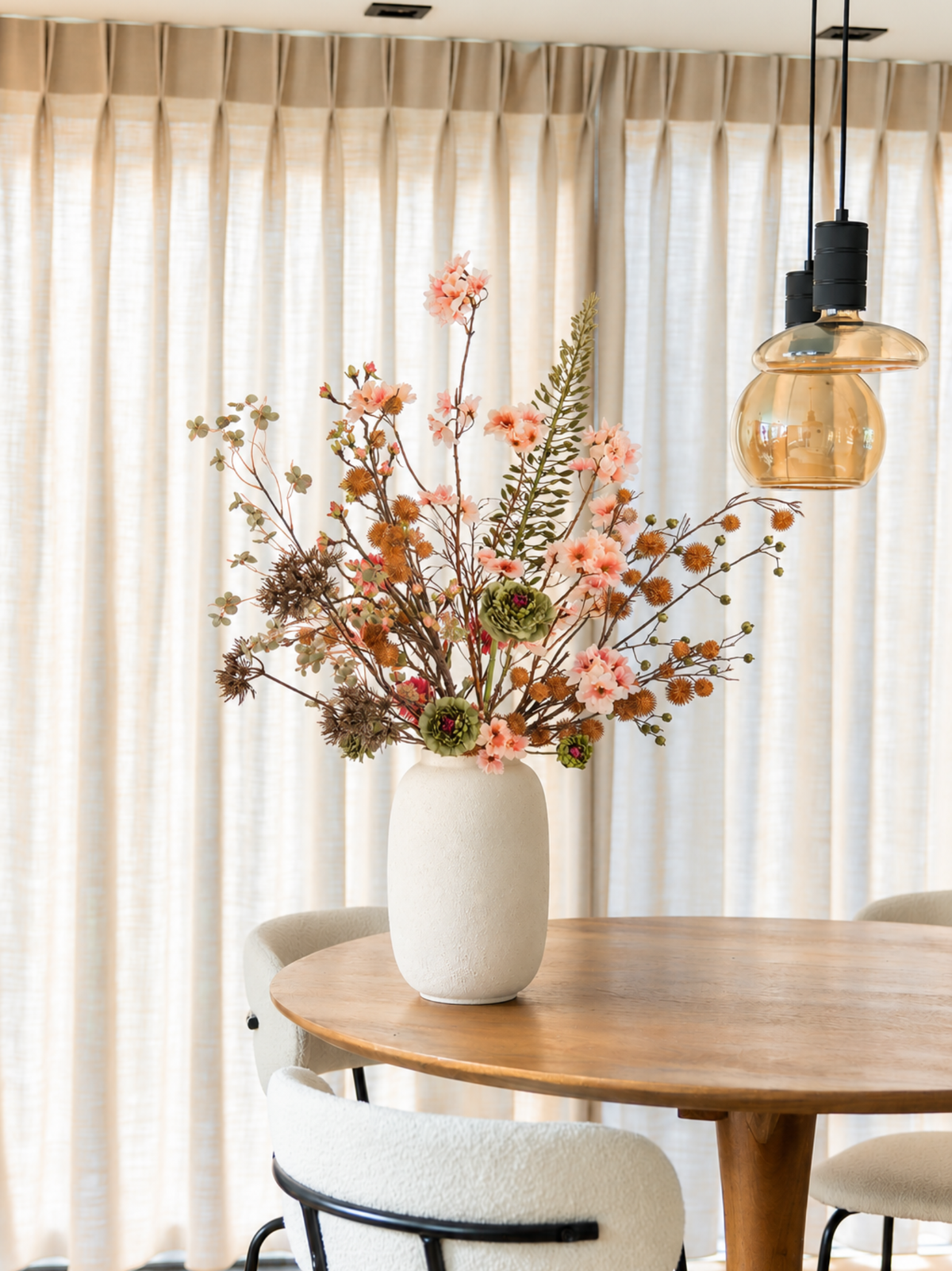 Kleurrijk kunstbloemen boeket Hazel met roze bloesemtakken, groene zijden bloemen en warme herfsttakken op een houten eettafel.