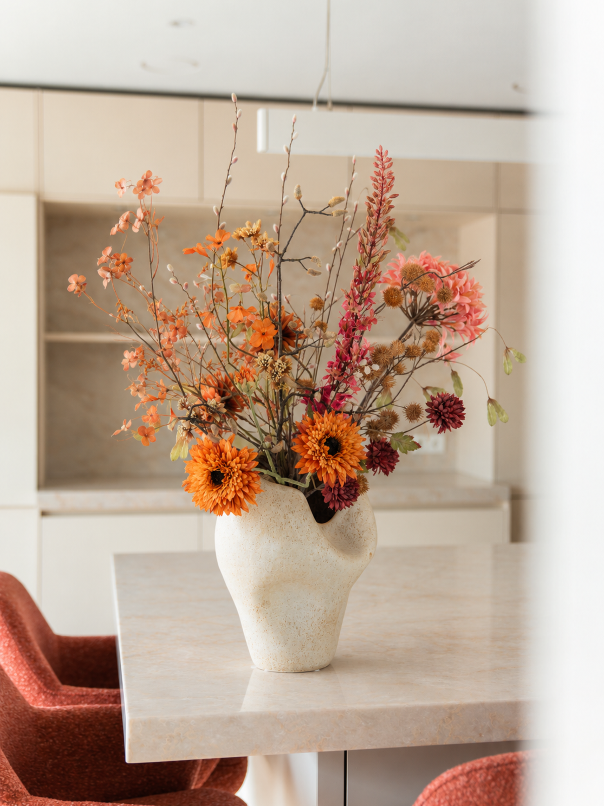 Kleurrijk kunstbloemen boeket Amber met oranje, oudroze en rode herfstbloemen op een eettafel in een modern interieur.