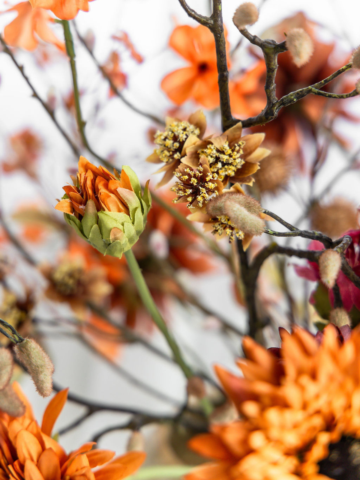 Detail van oranje zijden bloemknoppen, palmkatjes en bruine herfsttakken in het kunstboeket Amber van Blossig Bloemen.
