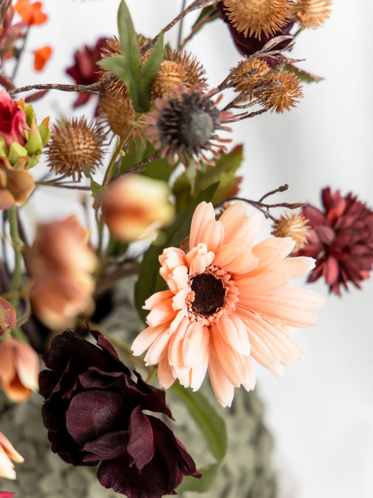 Close-up van perzikkleurige gerbera, donkerrode kunstbloemen en bruine herfsttakken in het kleurrijke zijden boeket Amelie.