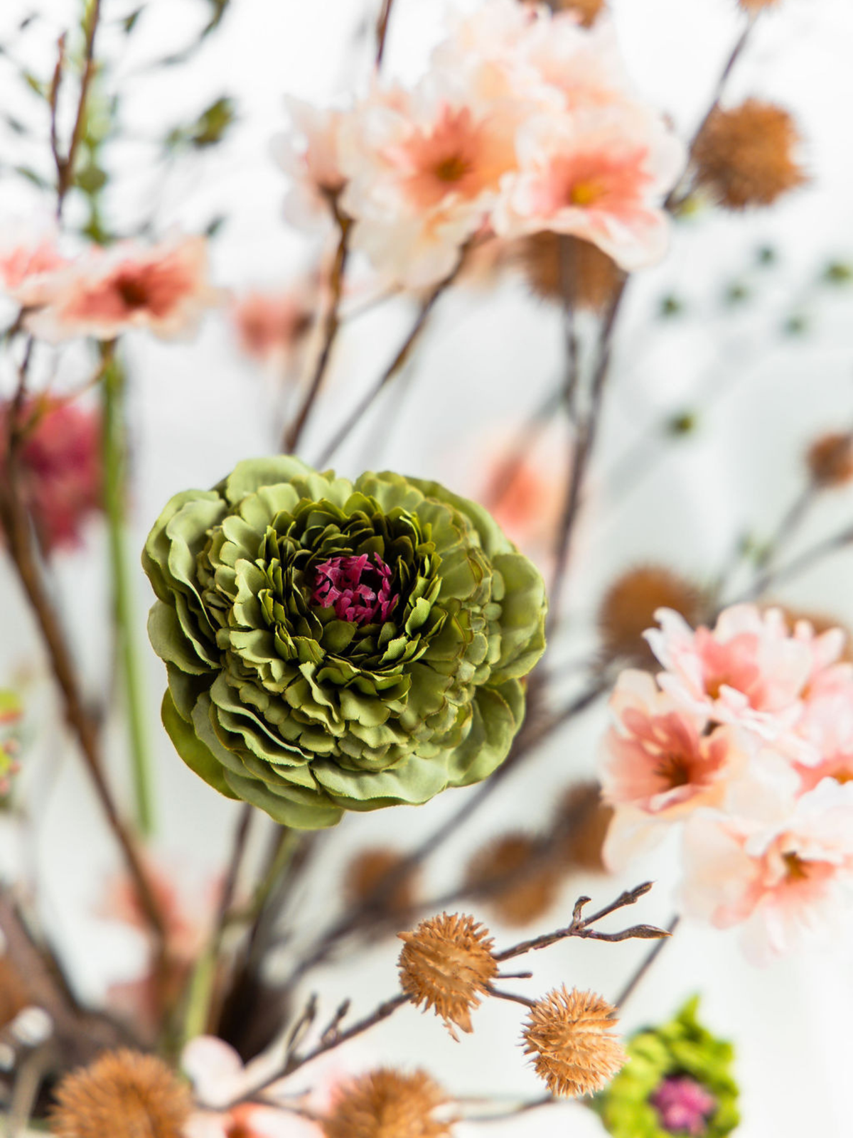 Close-up van groene zijden zinnia met donkerroze hart, oudroze kunstbloemen en bruine kastanjetakken in boeket Hazel.